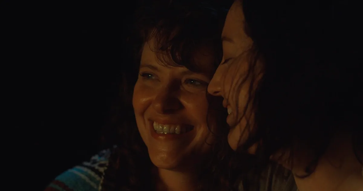 Two women laughing together in warm, low light.
