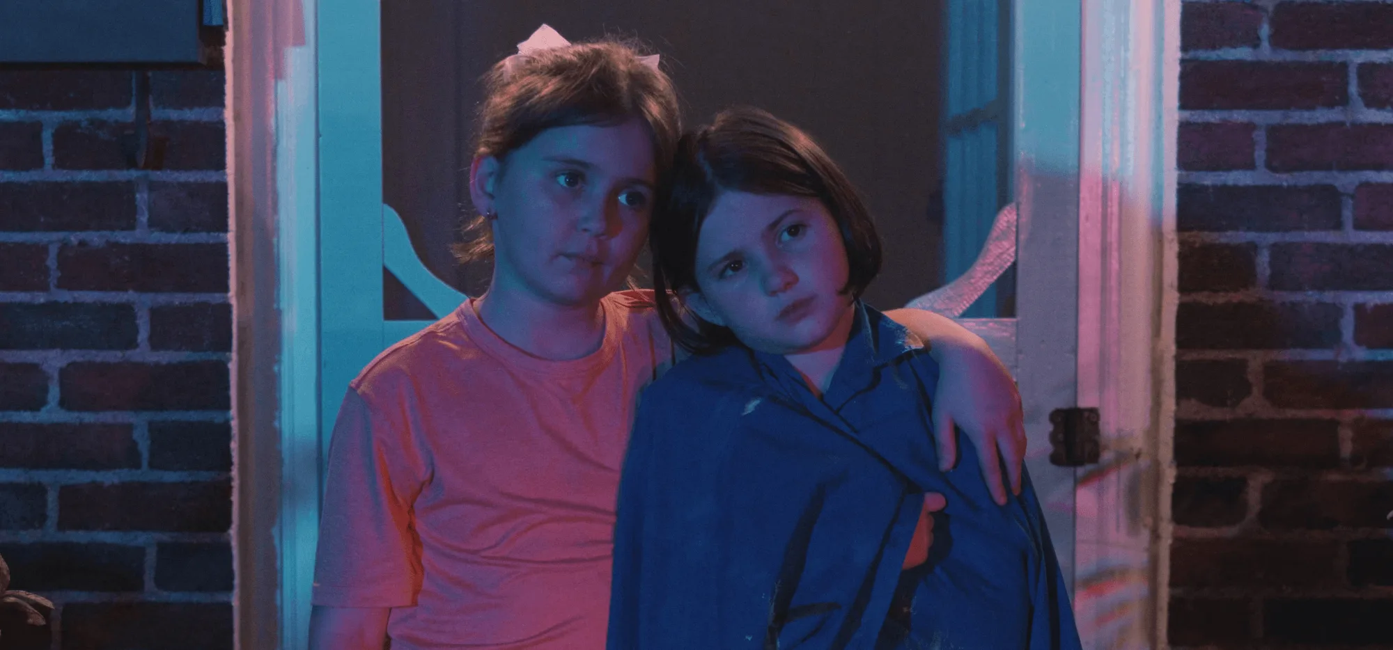 Two girls resting their foreheads together, lit in cool blue light.