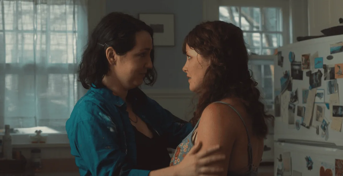 Two women holding each other in a sunlit kitchen.