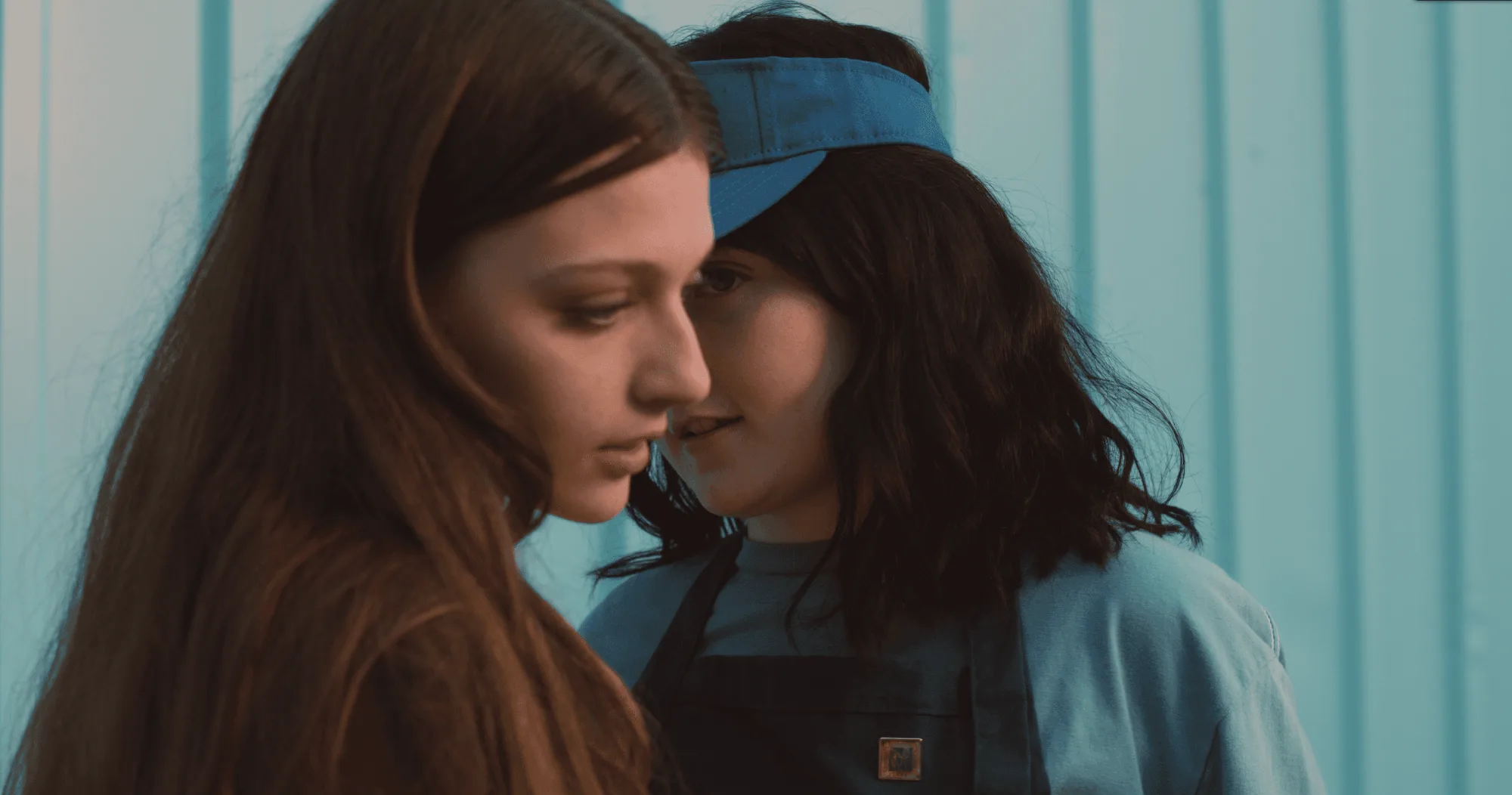 Two young girls standing close in a doorway at night, lit pink and blue.
